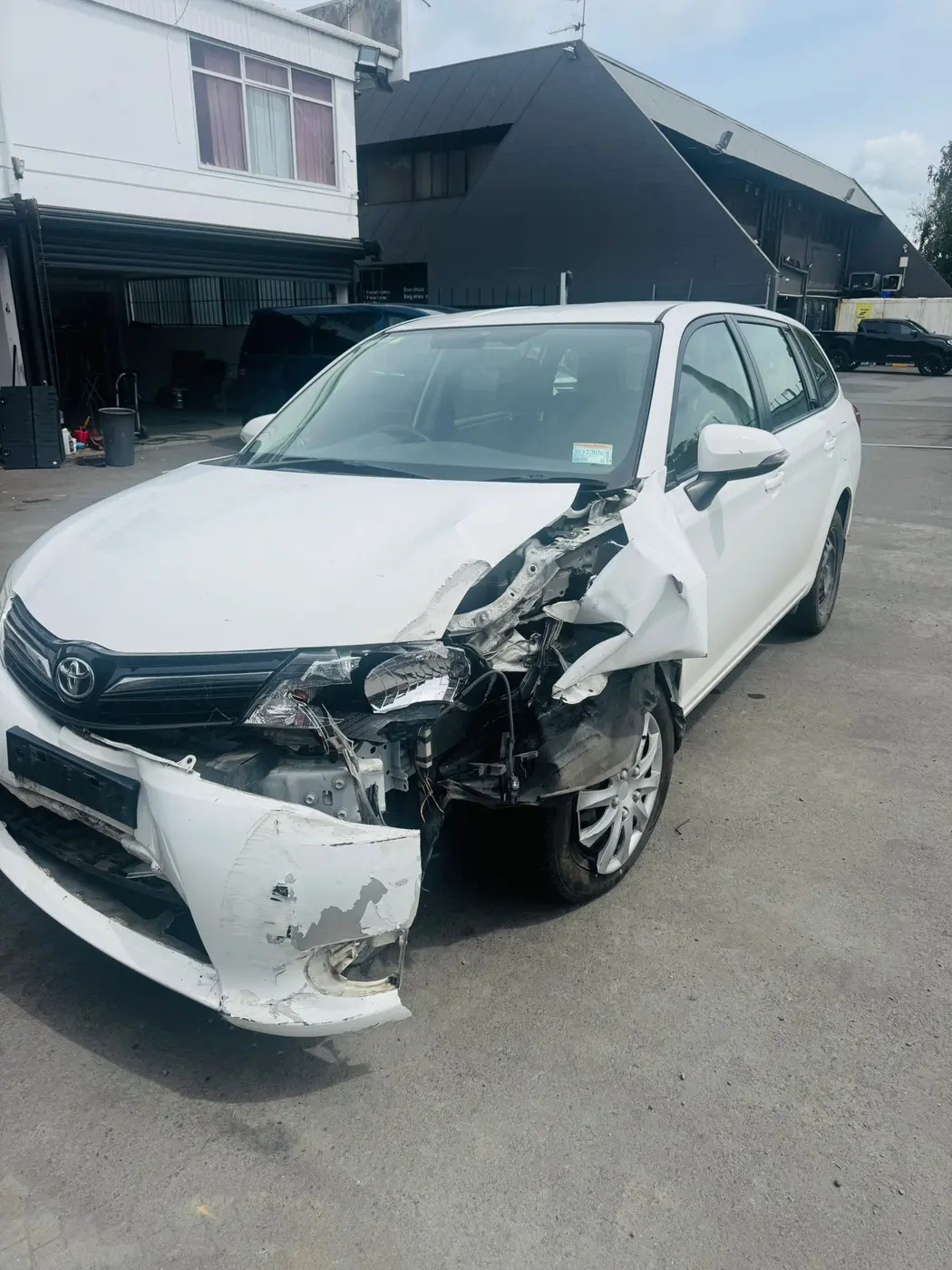 Accident-damaged white Toyota wagon with a smashed front